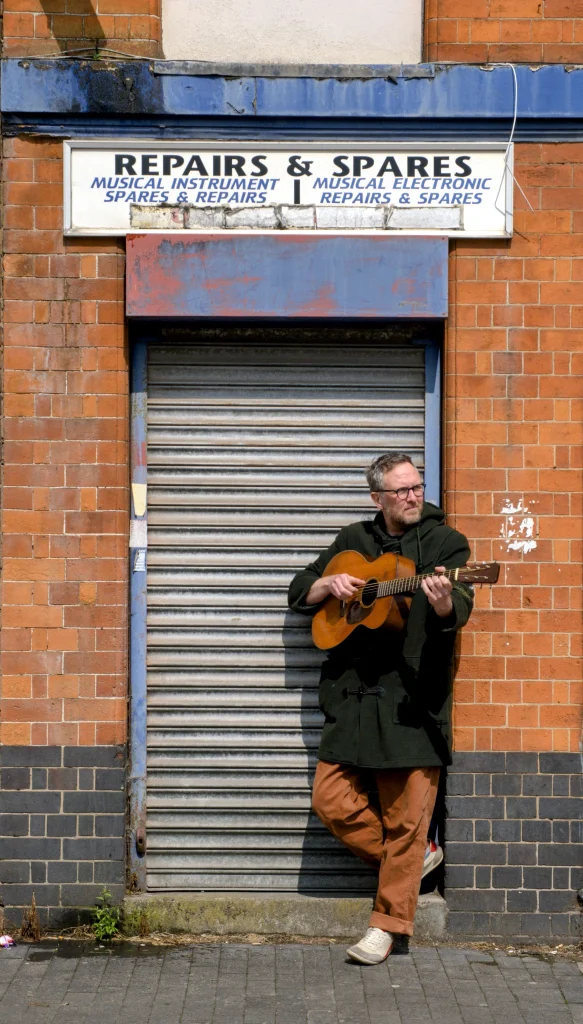 Jon Wilks leaning in a doorway playing a guitar